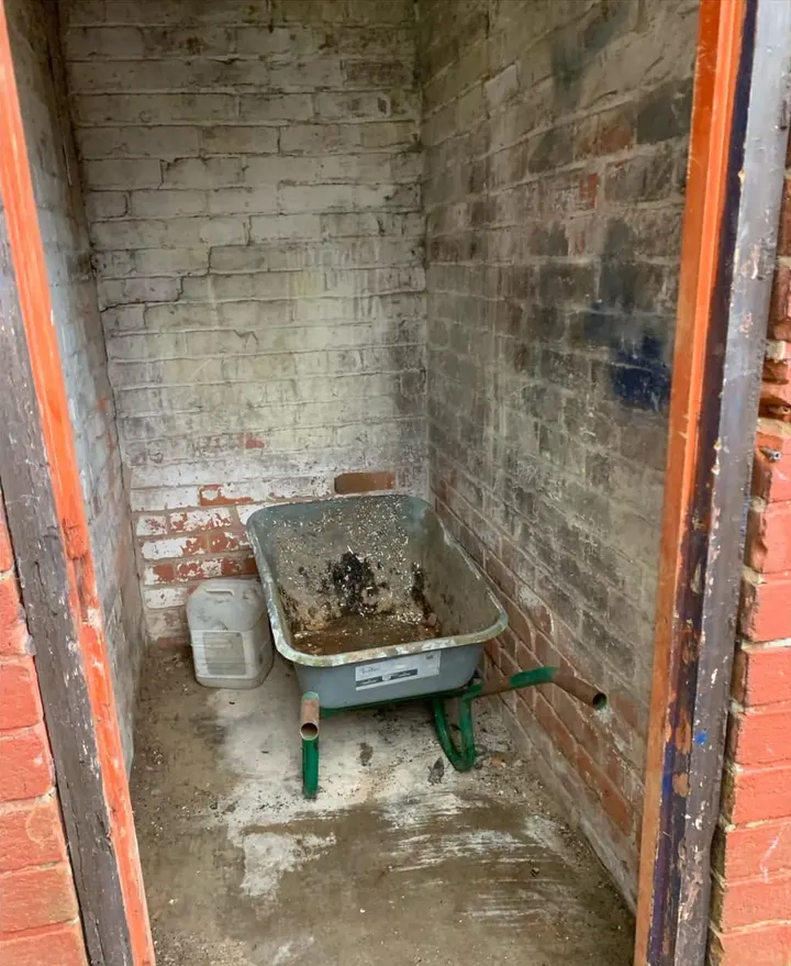 After: an empty brick outhouse with just a wheelbarrow inside