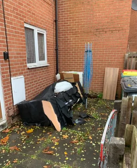 Before: a broken black sofa, boxes and a board in a small courtyard