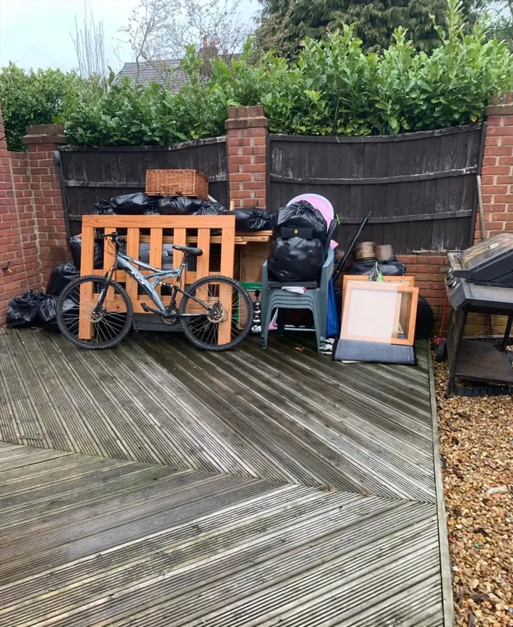 Before: bin bags, a bike, a cot, chairs and a barbecue piled on garden decking